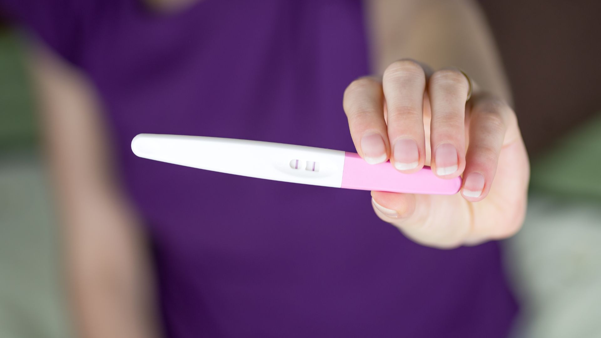 Woman holding a positive pregnancy test result after trying to conceive with a chronic illness.