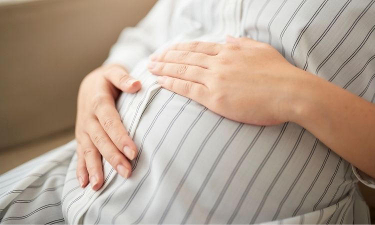 pregnant woman sitting quietly with hands on her bump, trusting her body during chronic illness pregnancy
