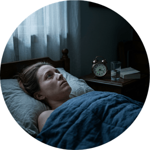 A woman lies awake in a dark bedroom at night, staring at the ceiling as moonlight falls across her face. An alarm clock reads 3:17am, capturing the exhaustion and alertness of chronic sleeplessness.