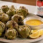 Lemon Artichokes on a plate with a citrus sauce and lemon wedges