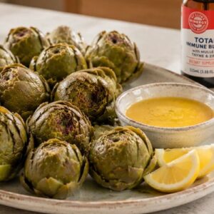 Lemon Artichokes on a plate with a citrus sauce and lemon wedges