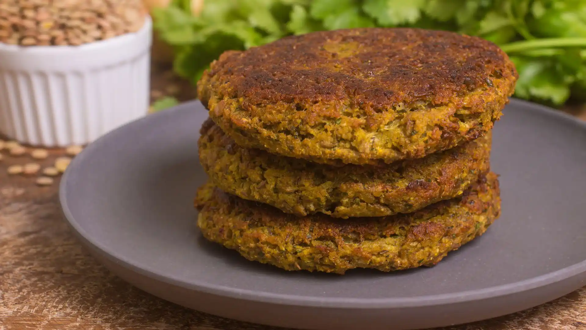 lentil mushroom burger patties stacked on a plate with cilantro and dried lentils in the background